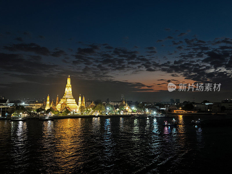 泰国曼谷，湄南河对岸的黎明寺(Wat Arun)，灯光照亮的滨水区，黄昏时水面的倒影，聚焦于前景